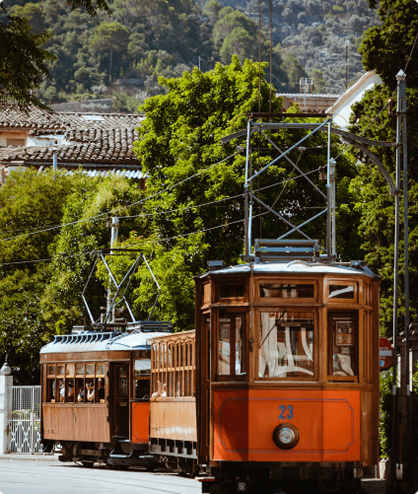 El emblemático tranvía vintage de madera atraviesa la histórica ciudad de Sóller, rodeada de exuberante vegetación y vistas a las montañas.